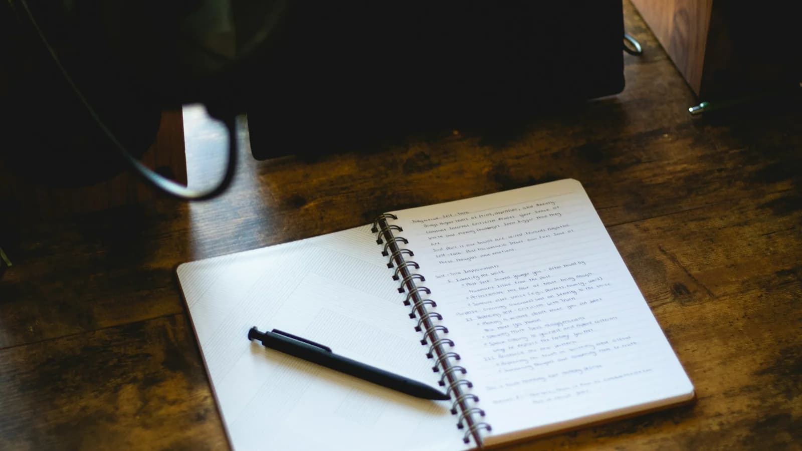 An open notebook with a pen resting on a wooden desk