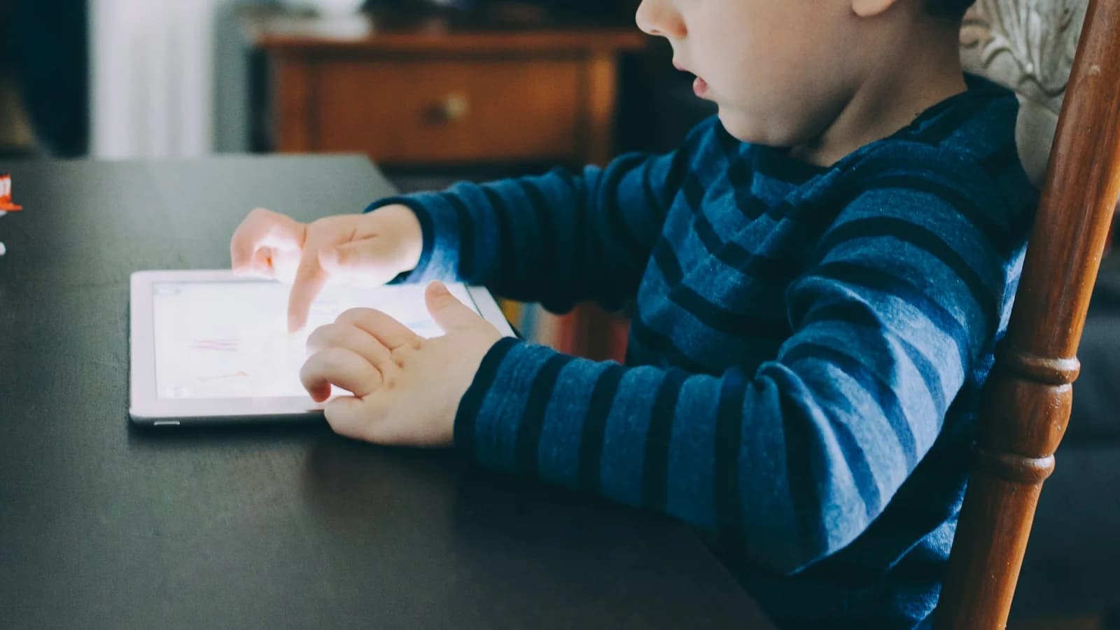 A young child sitting at a table using a tablet
