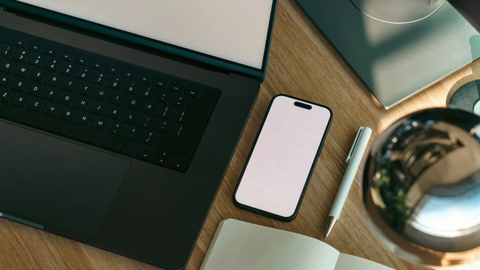 A laptop, phone, and notebook arranged on a wooden desk