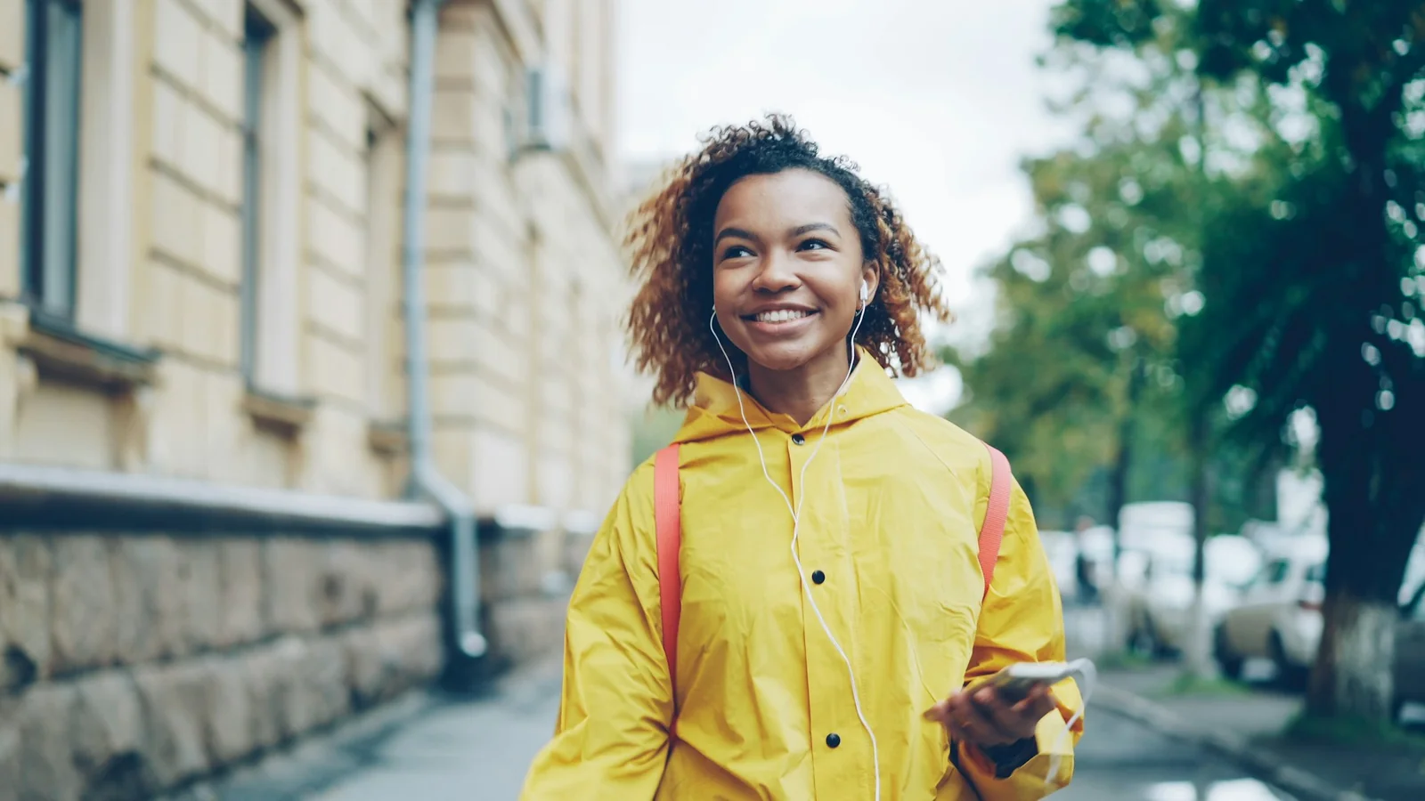 A young person walking down a street wearing yellow coat and headphones