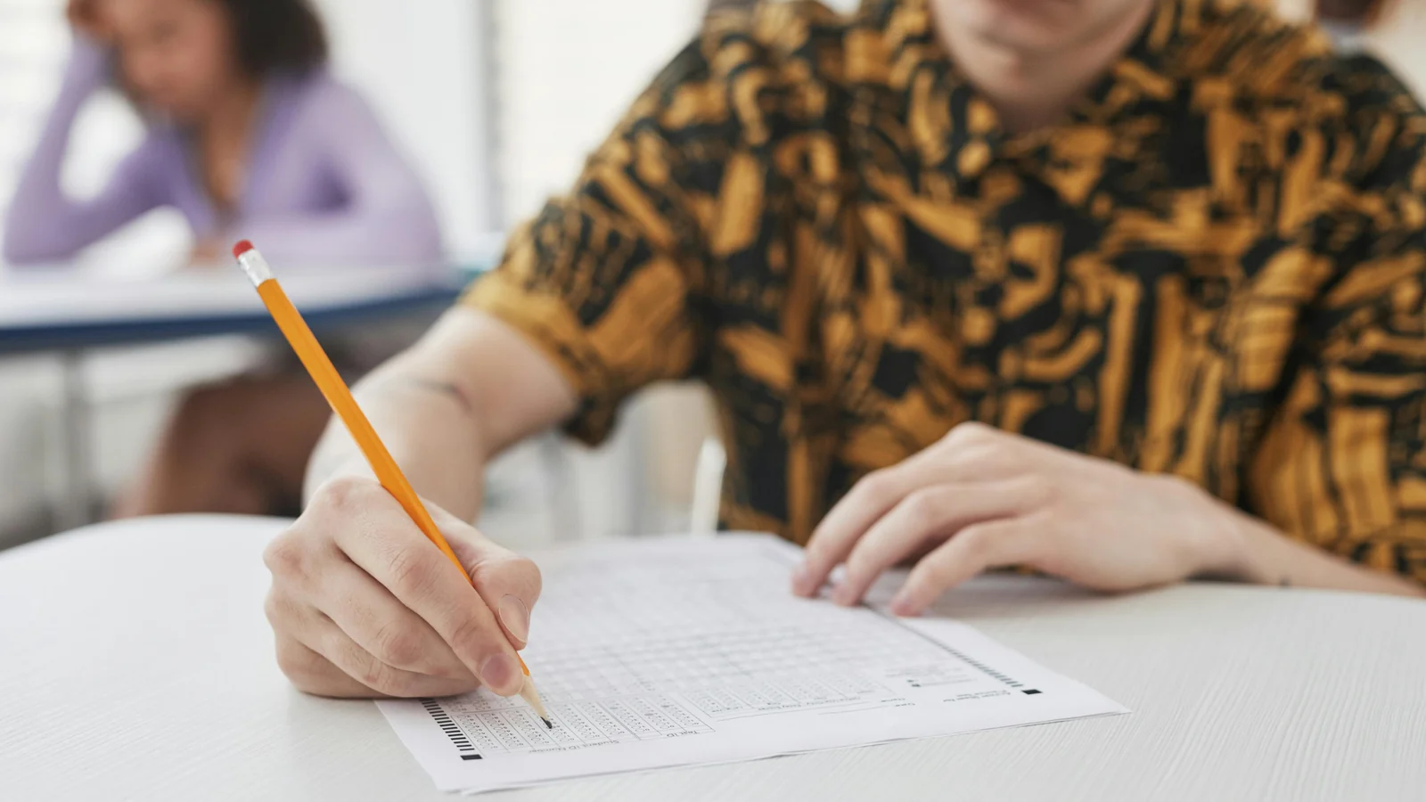A student holding a pencil while writing on a sheet of paper