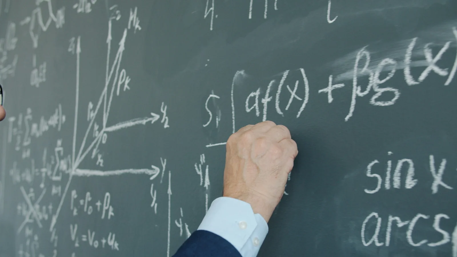 A teacher writing mathematical formulas on a blackboard