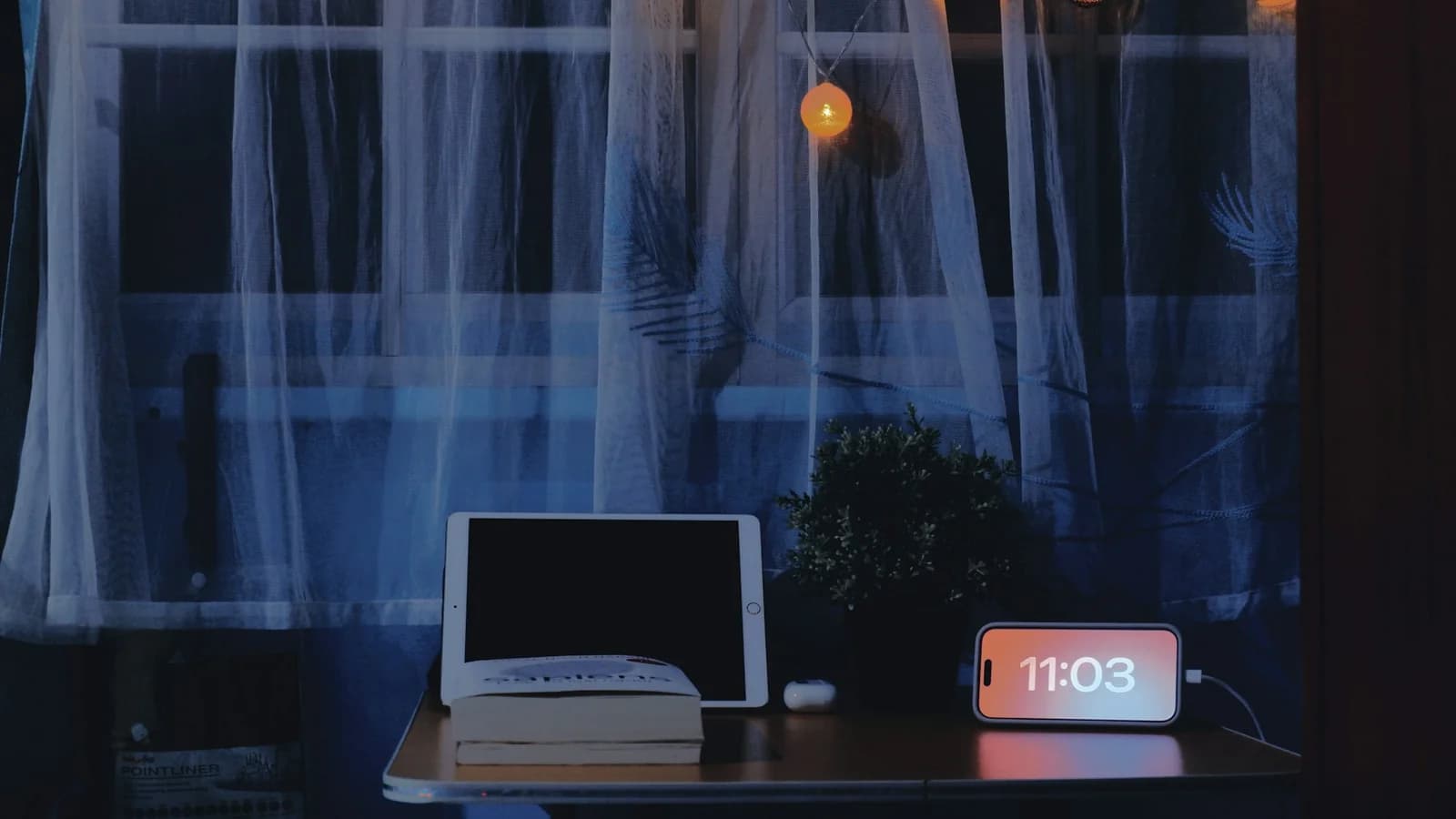 A study desk at night with a digital clock, tablet and book