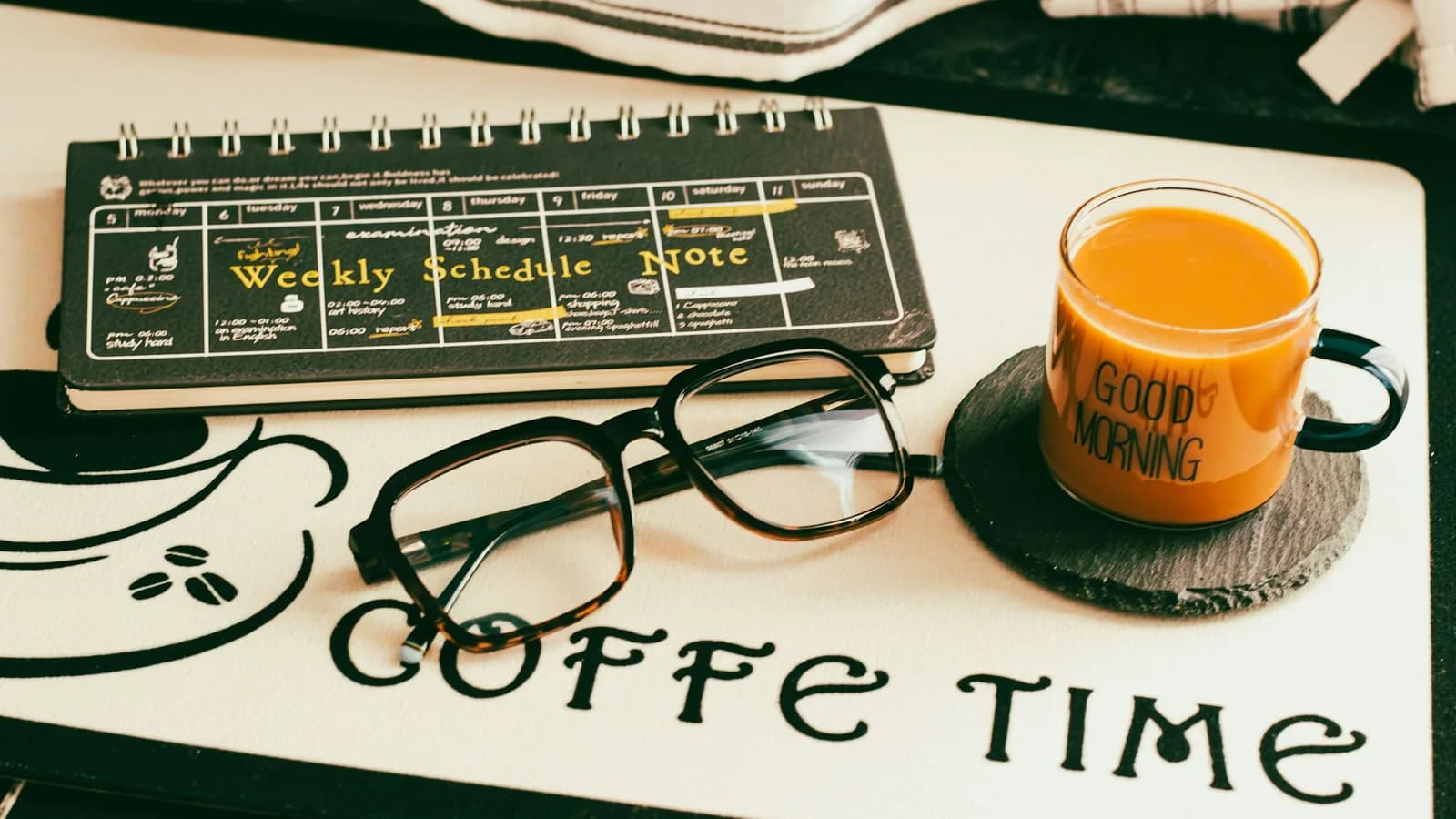 A morning study setup with a coffee mug, glasses, and a planner on a wooden desk