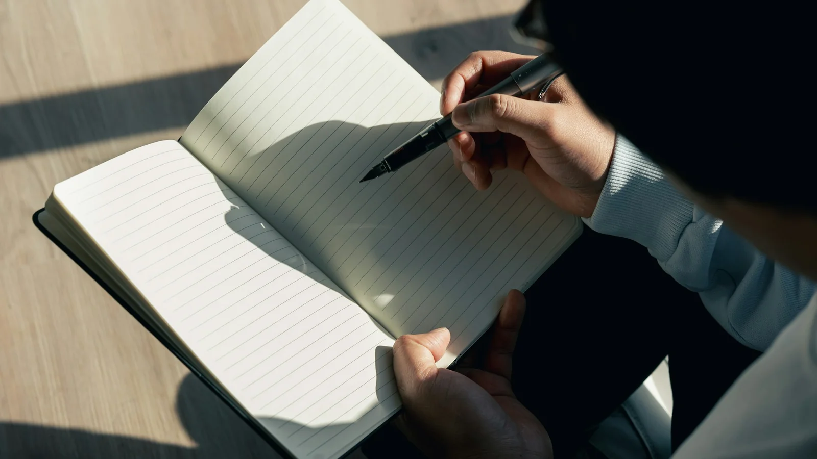 A person sitting and writing notes in a journal at a wooden desk