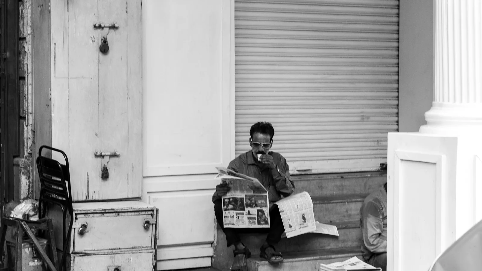 A man sitting on outdoor steps, reading a folded newspaper in the morning light